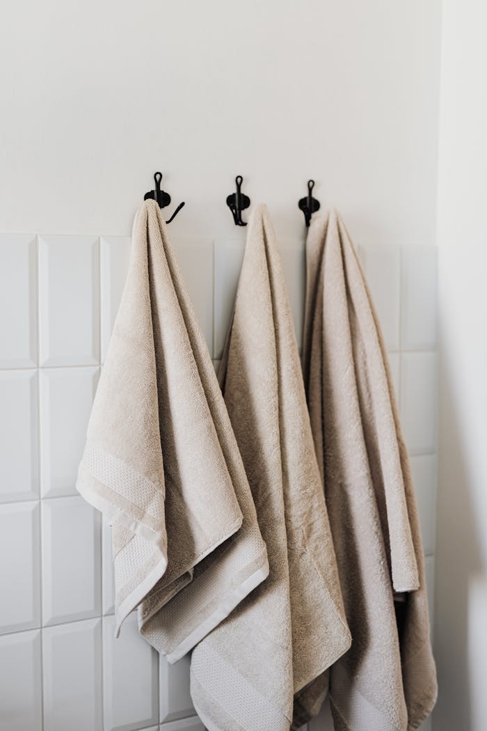 Beige hand towel and face towel and floor towel hooked in bathroom against white tiles in hotel room